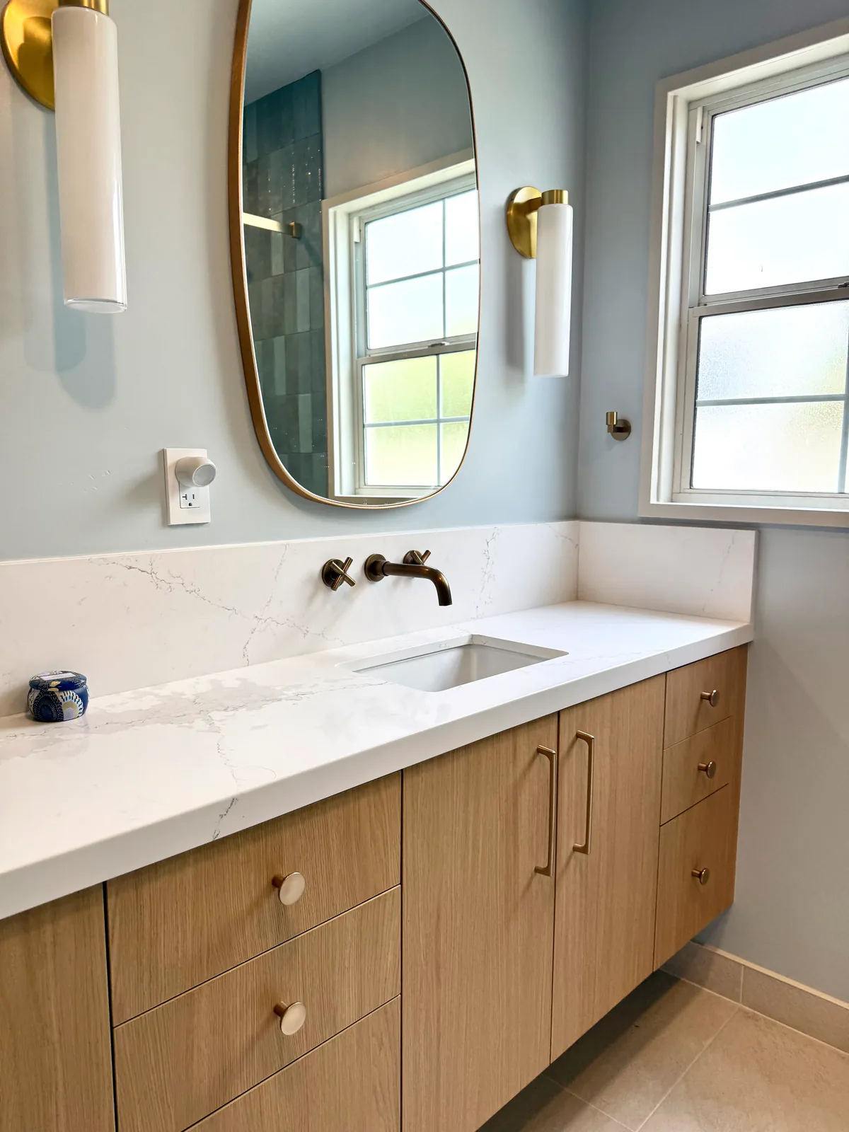 Single vanity with oval mirror beside a frosted window