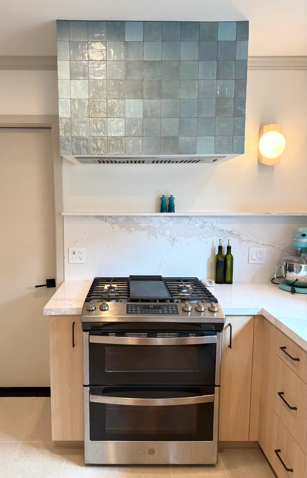 Gas range under a hand-glazed blue tile hood with quartz slab backsplash